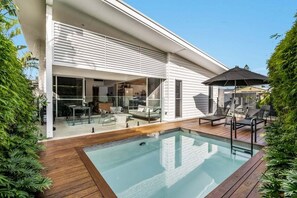 A modern house with a swimming pool, outdoor seating, and a covered patio area. - Enjoy the deluxe swimming pool surrounded by a poolside sundeck (Lennox Head)