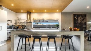 A modern kitchen with a central island, bar stools, and a large window. - Enjoy the deluxe swimming pool surrounded by a poolside sundeck (Lennox Head)