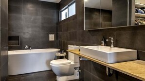 A modern bathroom with a freestanding bathtub, a toilet, and a large mirror above the sink. - Enjoy the deluxe swimming pool surrounded by a poolside sundeck (Lennox Head)