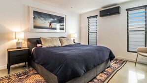 A bedroom with a bed, bedside lamps, a wall-mounted TV, and a window with blinds. - Enjoy the deluxe swimming pool surrounded by a poolside sundeck (Lennox Head)
