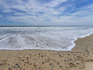 Une plage où les vagues viennent doucement lécher le rivage, parsemée de galets, et un ciel dégagé.