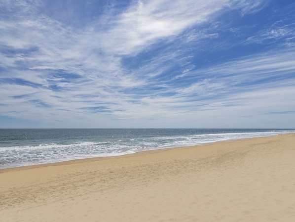 Una playa con una extensa orilla arenosa y un cielo azul despejado con algunas nubes.