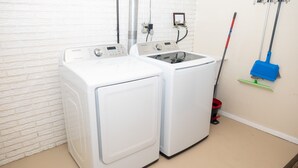 Ein Waschbereich mit zwei weißen Waschmaschinen, einem Mop und einem Besen, der an der Wand angelehnt ist.