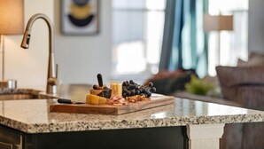 A kitchen counter with a marble top, a cutting board with cheese, grapes, and nuts, and a sink with a faucet.
