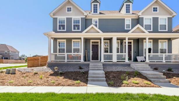A two-story house with a front porch, a small front yard, and a clear sky.