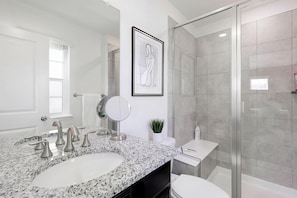 Une salle de bain moderne avec un comptoir en granit, un grand miroir, une œuvre d’art encadrée et une cabine de douche en verre.