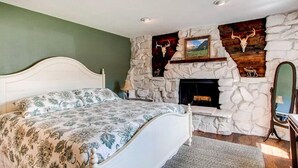A bedroom with a stone fireplace, a bed with floral bedding, and a painting above the fireplace. - Hidden Valley Retreat. Foothill views. Large Yard! (Loveland)