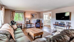 A living room with a sofa, a coffee table, a chair, a TV, and a painting on the wall. - Hidden Valley Retreat. Foothill views. Large Yard! (Loveland)