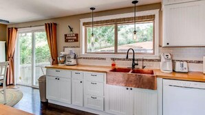A kitchen with white cabinets, a copper sink, and a window with a view of greenery. - Hidden Valley Retreat. Foothill views. Large Yard! (Loveland)