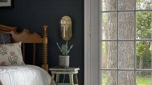 Un dormitorio con una cama, una mesita con una planta, una lámpara de pared y un ventanal con vistas a árboles.