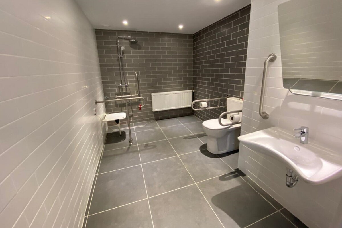 Een moderne badkamer met grijze betegelde wanden, een wit toilet, een bidet, een wastafel en een bad.