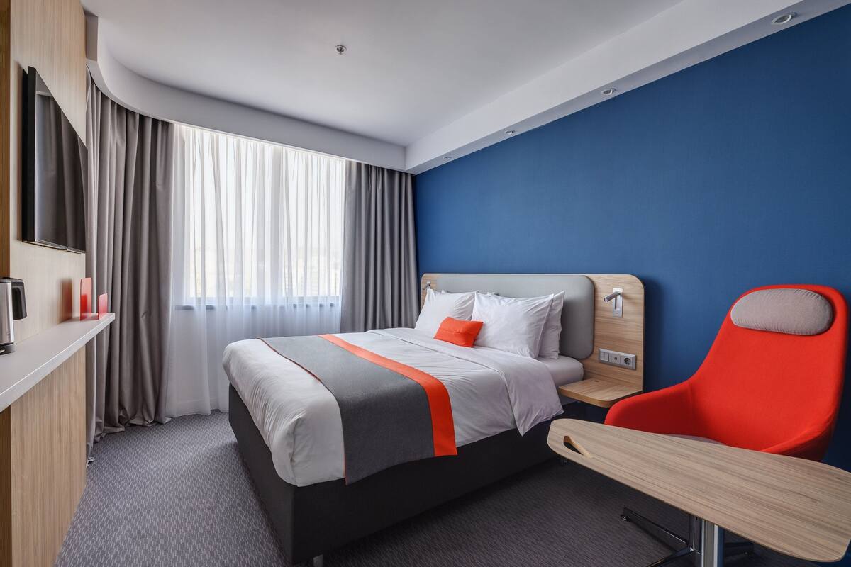 A hotel room with a bed, a desk, a chair, a TV, and curtains.