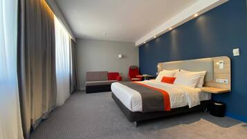 Una camera d'albergo moderna con un letto grande, un divano, una poltrona rossa e una scrivania.