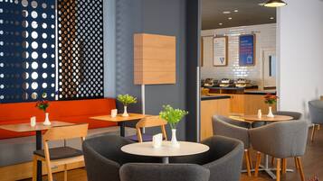 Een modern café met ronde tafels, grijze stoelen en oranje zitplaatsen.