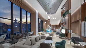 A modern lounge area with sofas, chairs, and tables, large windows offering a city view, and a unique ceiling design. - Holiday Inn Luzhou Longjian by IHG (Luzhou)
