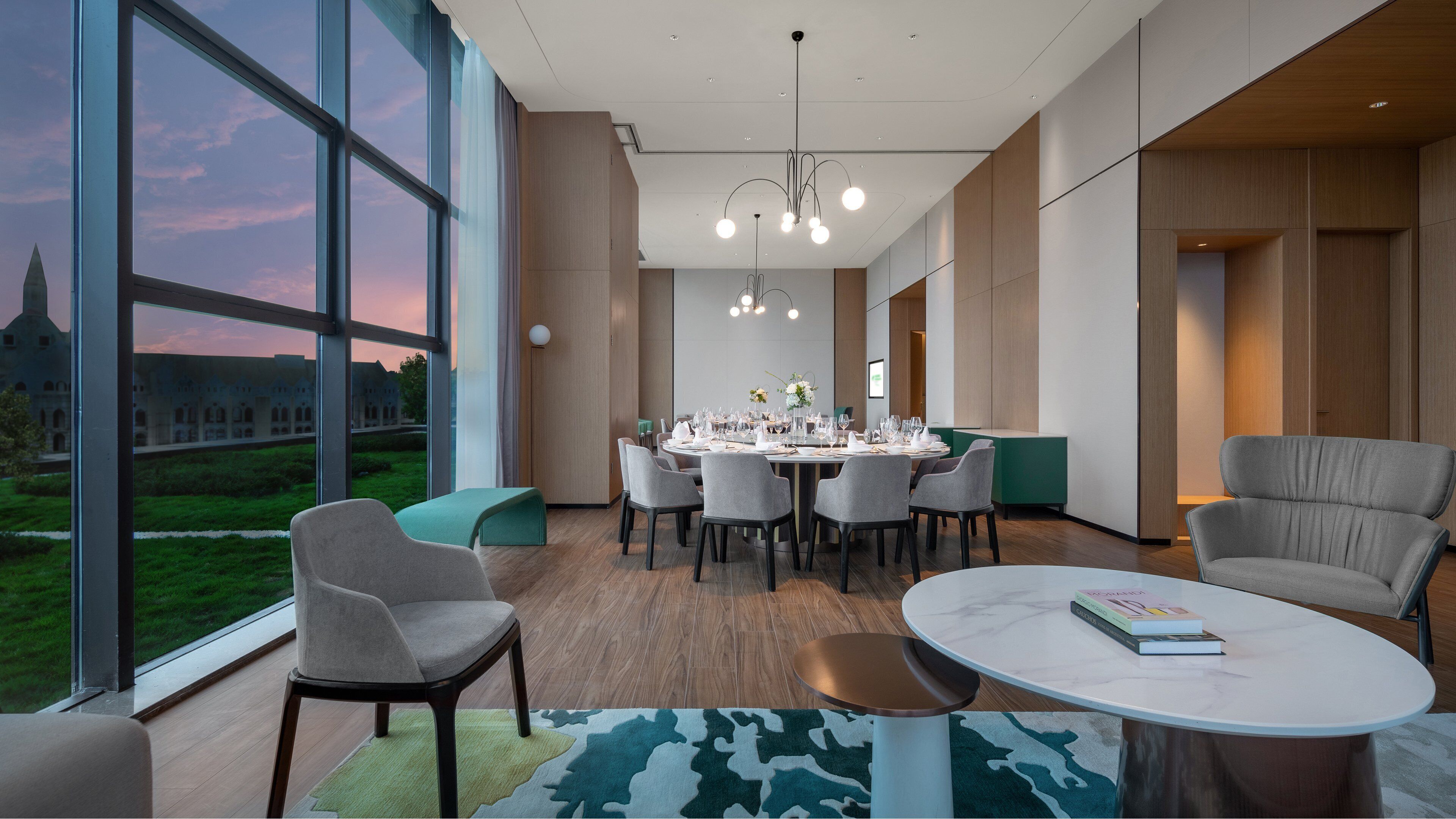 Un comedor moderno con una mesa grande dispuesta para una comida, rodeada de sillas, y vistas a un edificio a través de amplios ventanales.