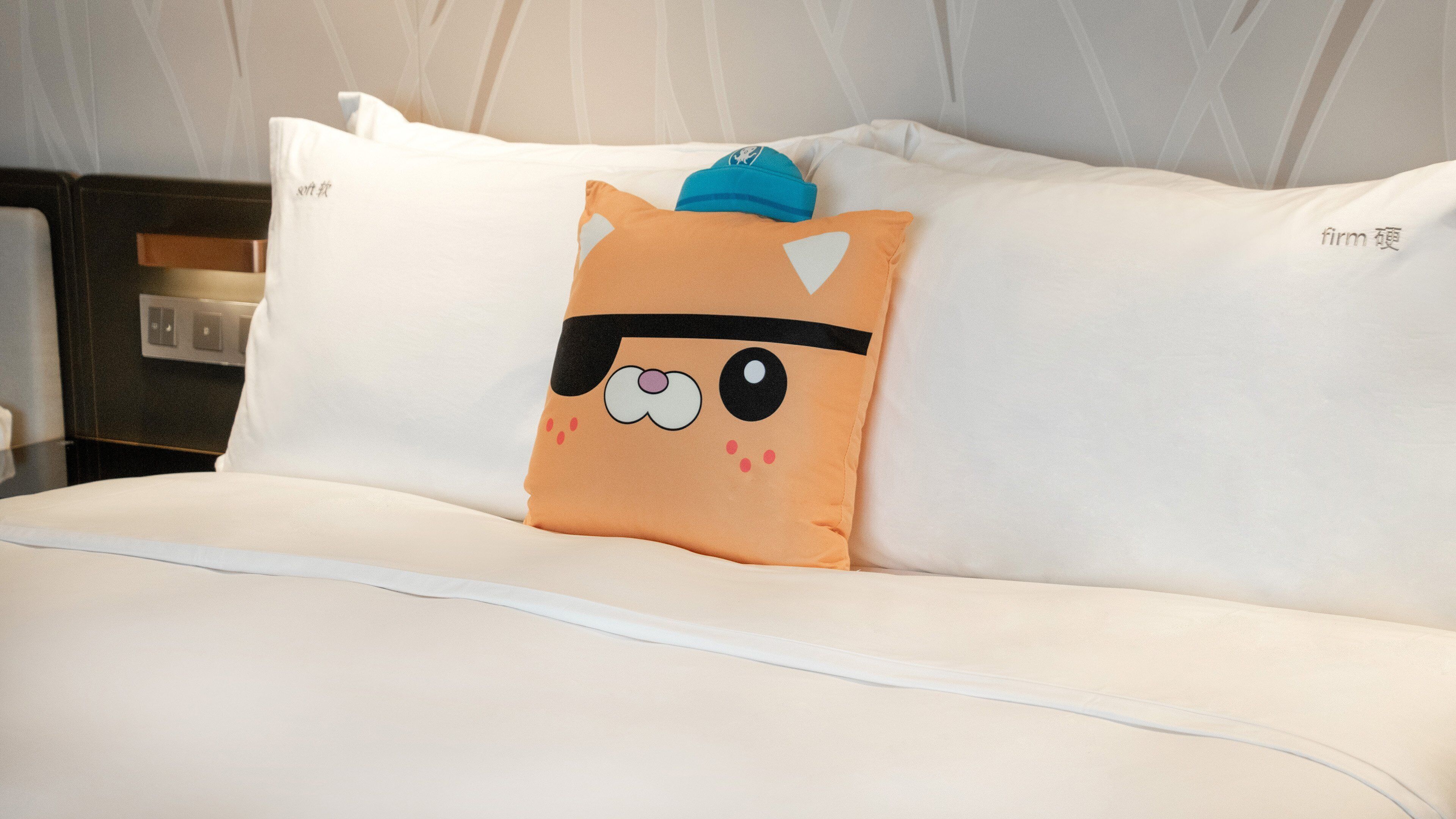 A bed with white bedding and a pillow featuring a cartoon cat design.