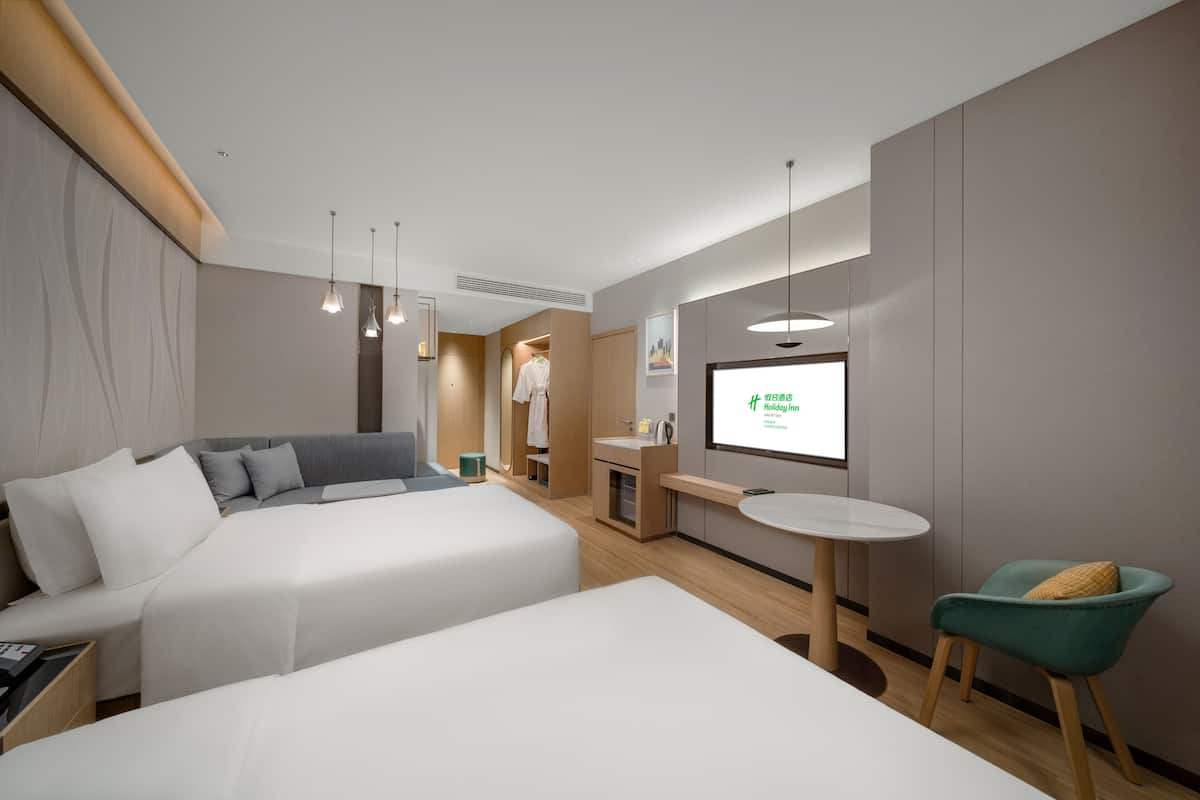 A modern hotel room with two beds, a small desk, a chair, and a TV displaying a screen.