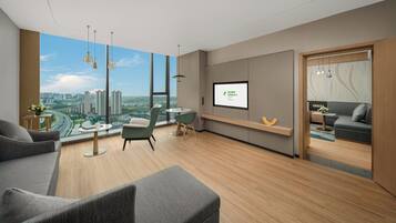 A modern hotel room with a large window, a sofa, a dining table, and a TV screen displaying the hotel name.