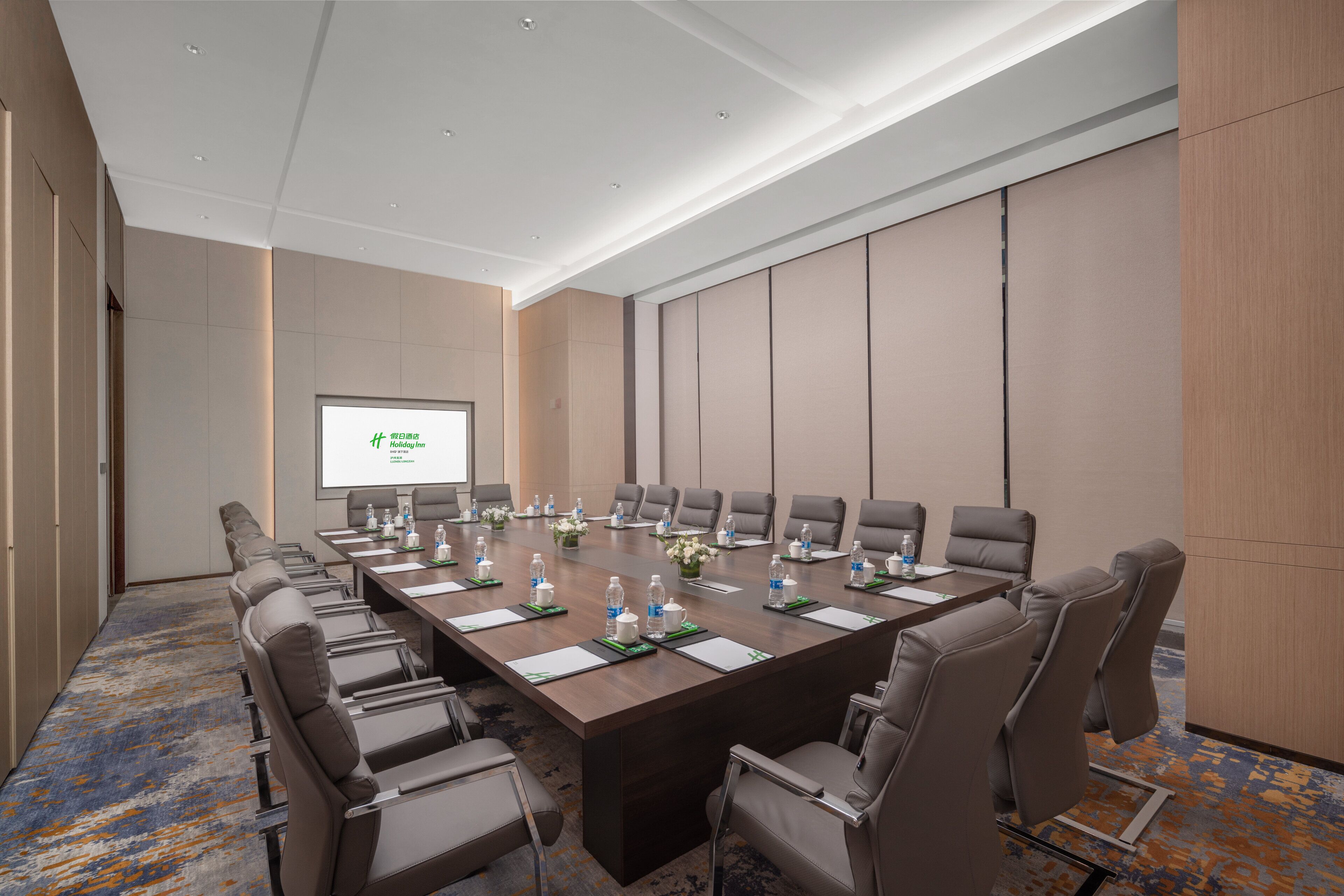 Una sala conferenze con un lungo tavolo, sedie, uno schermo per proiettore e un pavimento rivestito di moquette.