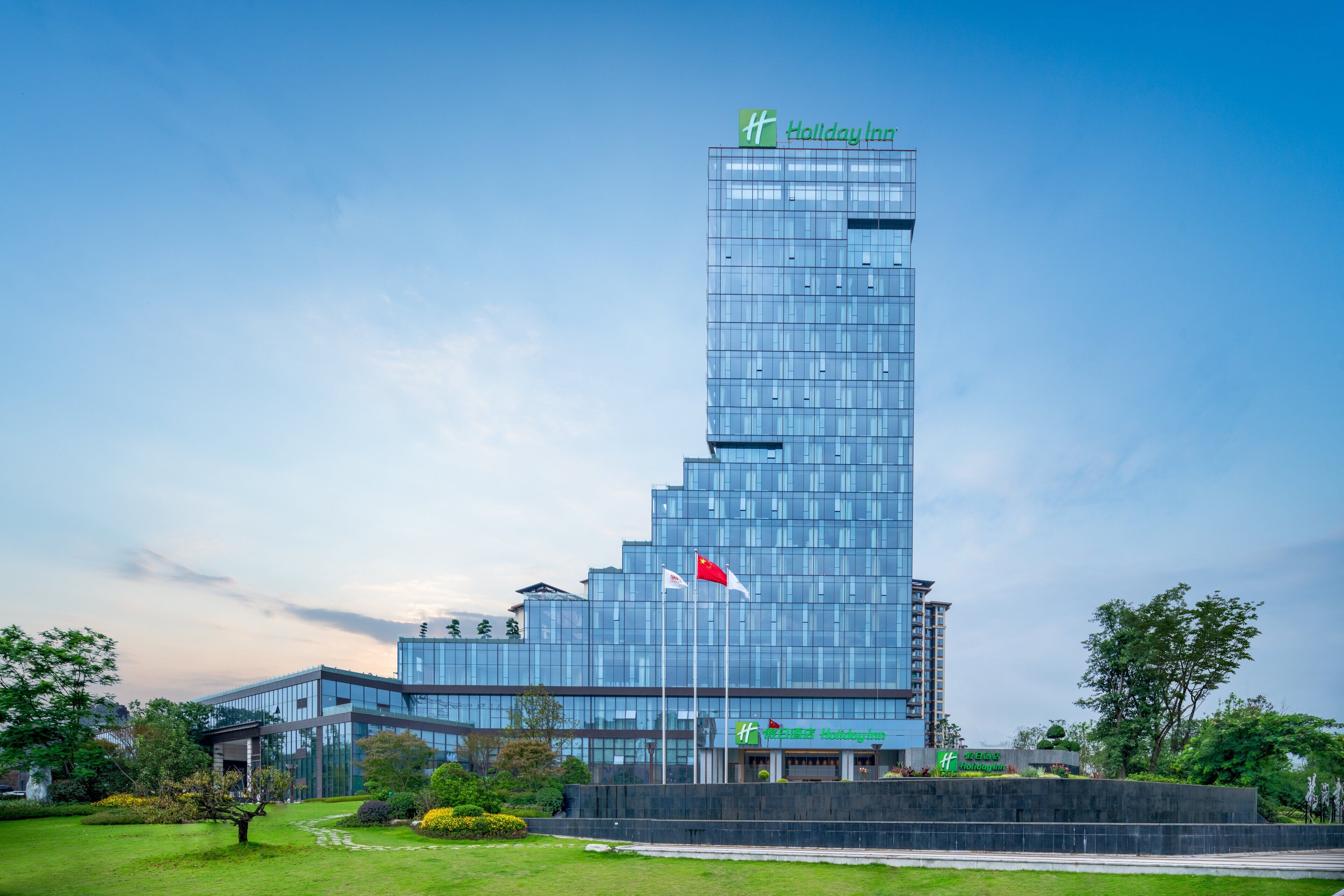 A modern Holiday Inn hotel with a glass facade, multiple floors, and a flagpole with flags.