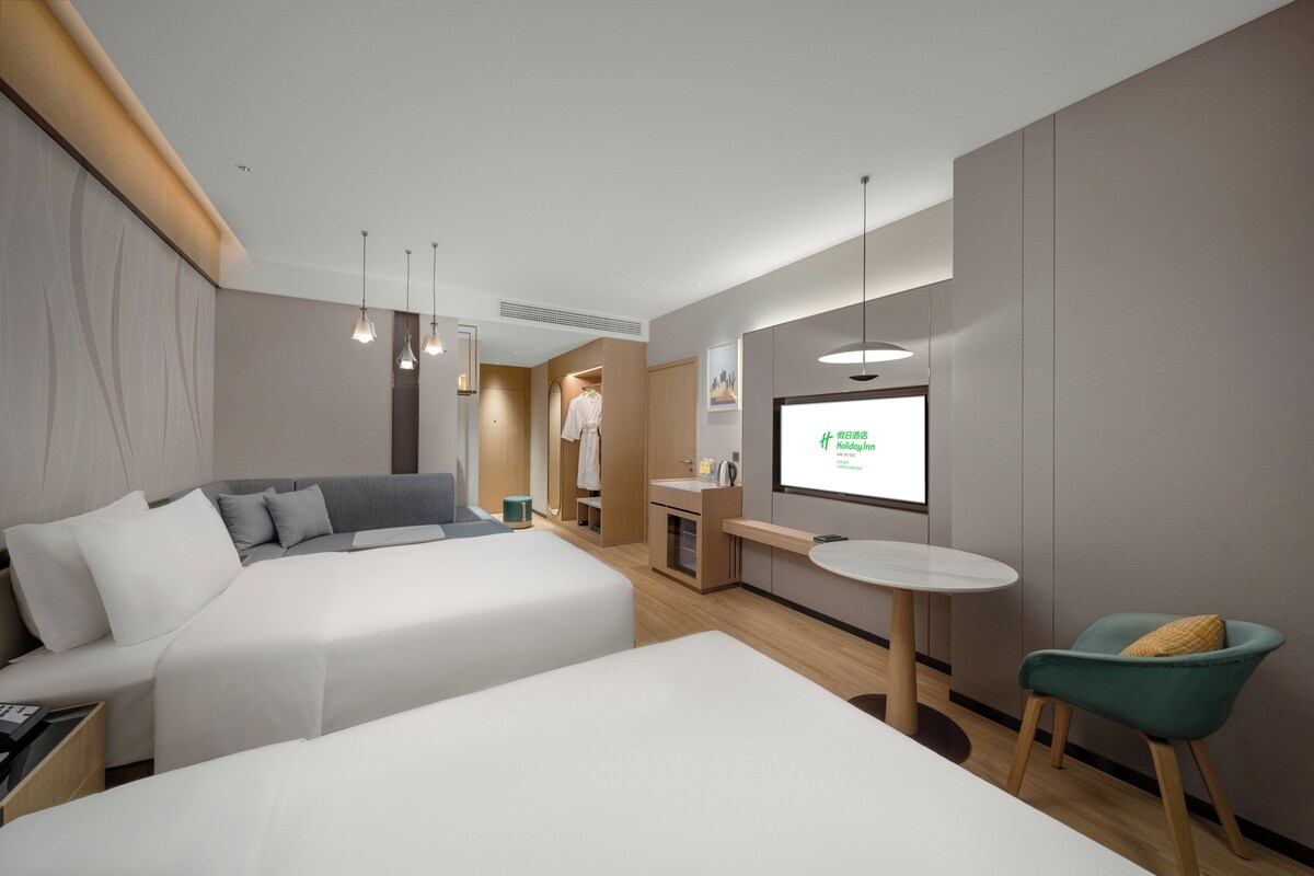 Ein modernes Hotelzimmer mit zwei Betten, einem kleinen Schreibtisch, einem Stuhl und einem Fernseher, der ein Bild zeigt.