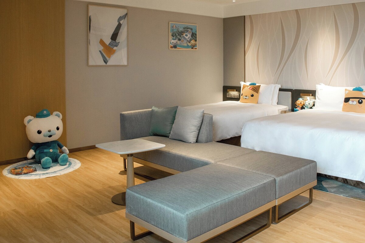 Ein modernes Hotelzimmer mit einer Couch, einem kleinen Tisch und einem Bett mit zwei Kissen.