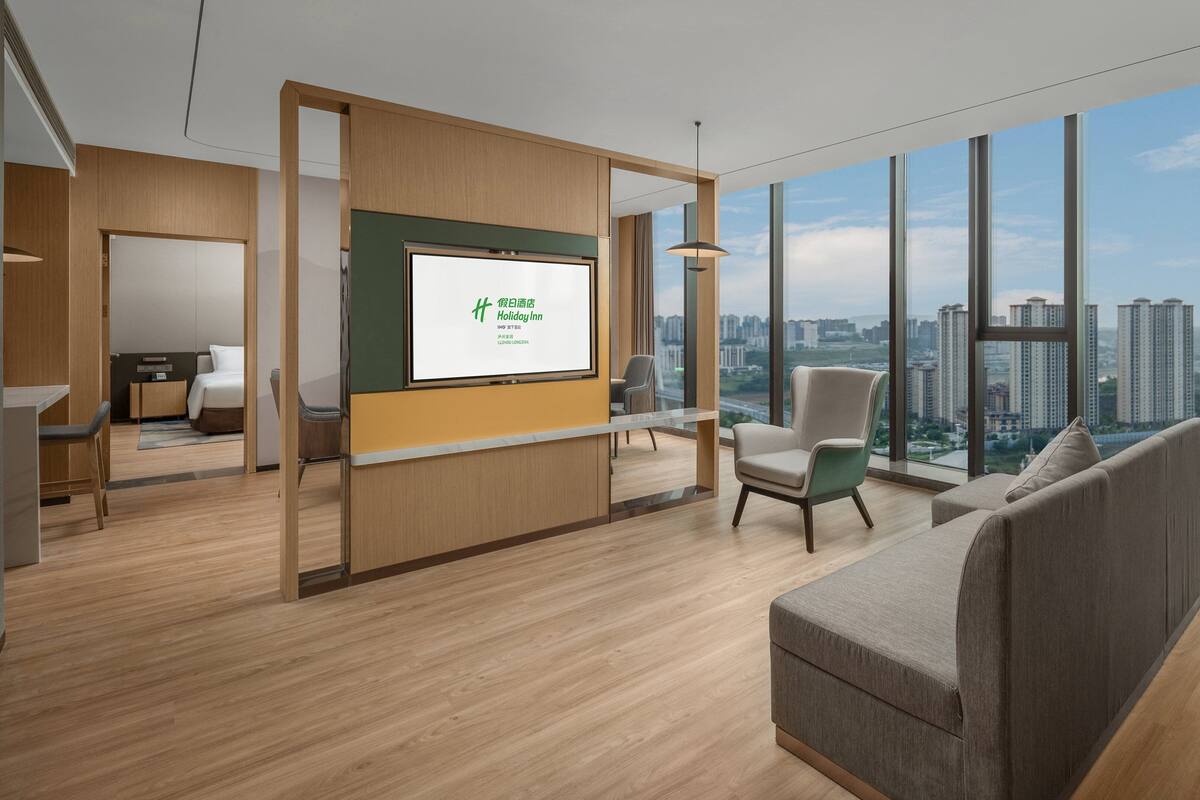 A modern hotel room with a large window offering a city view, a comfortable sofa, a desk, and a bed.