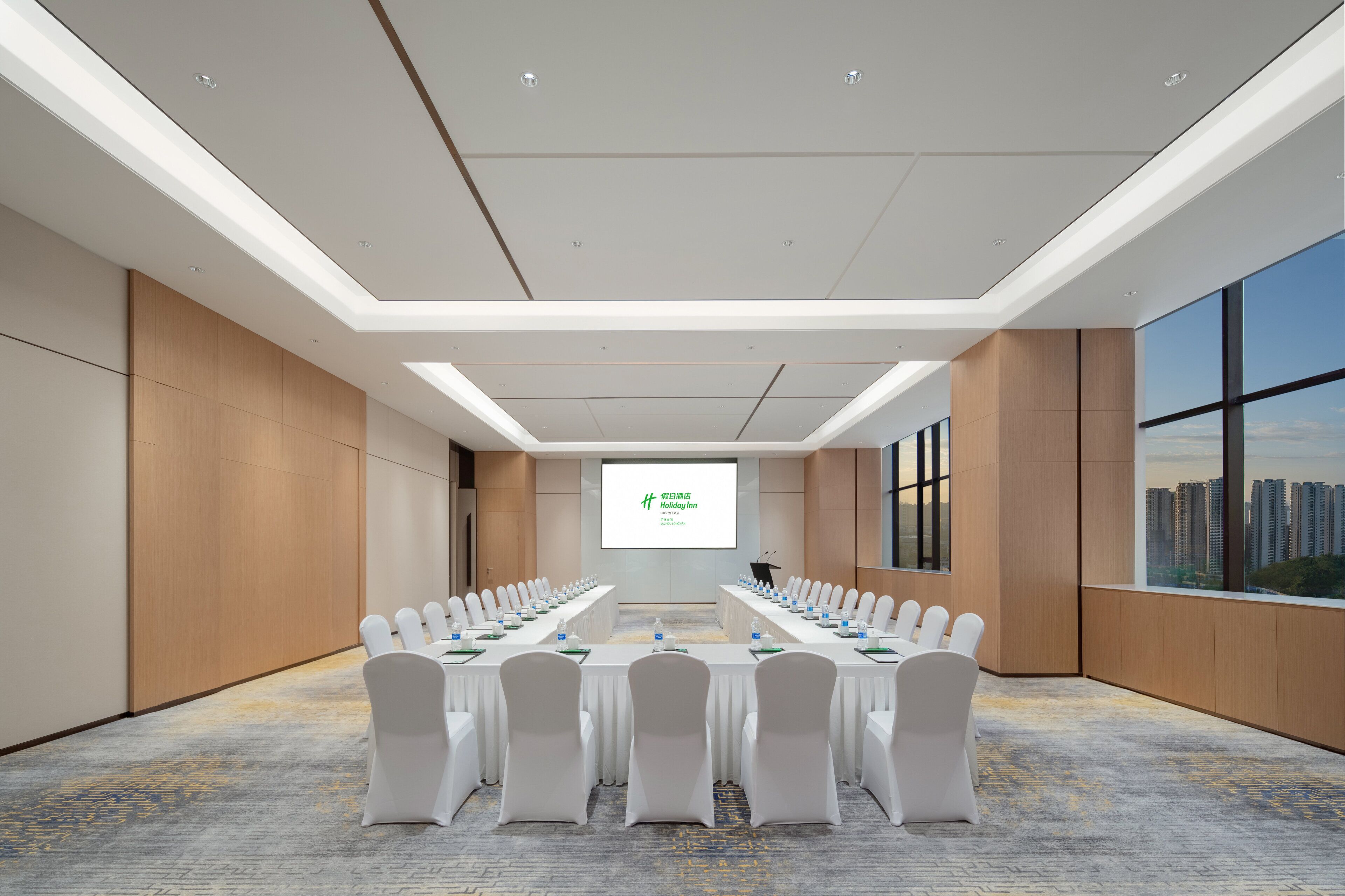 Un salón de conferencias con una mesa larga, sillas blancas y una pantalla de presentación.