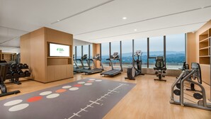 A modern gym with treadmills, weights, and a large screen displaying a logo. - Holiday Inn Luzhou Longjian by IHG (Luzhou)