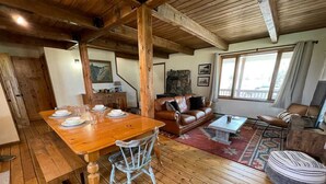A wooden dining table set with plates and glasses, a leather sofa, and a coffee table in a room with wooden floors and a stone fireplace. - Private Ranch Property Minutes to Yellowstone NP (Gardiner)