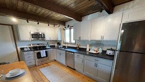 A modern kitchen with white cabinets, stainless steel appliances, and a wooden dining table set for two. - Private Ranch Property Minutes to Yellowstone NP (Gardiner)