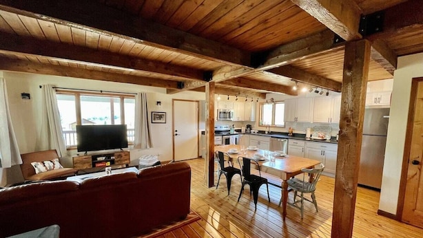 A spacious living area with a wooden floor, a sofa, a television, and a dining table with chairs. - Private Ranch Property Minutes to Yellowstone NP (Gardiner)