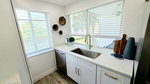A kitchen with white cabinets, a stainless steel sink, and a window with blinds. - POSHPADZ Kai Villa-Water Views, Balcony, Walk to Jupiter Beach Sleeps 4 (Jupiter)