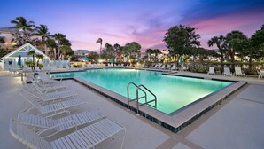 A swimming pool with lounge chairs and a small building, surrounded by palm trees and buildings in the background. - POSHPADZ Kai Villa-Water Views, Balcony, Walk to Jupiter Beach Sleeps 4 (Jupiter)