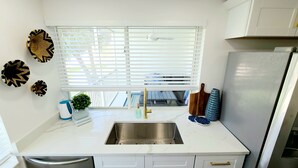 A kitchen with a white countertop, stainless steel sink, and a refrigerator. - POSHPADZ Kai Villa-Water Views, Balcony, Walk to Jupiter Beach Sleeps 4 (Jupiter)