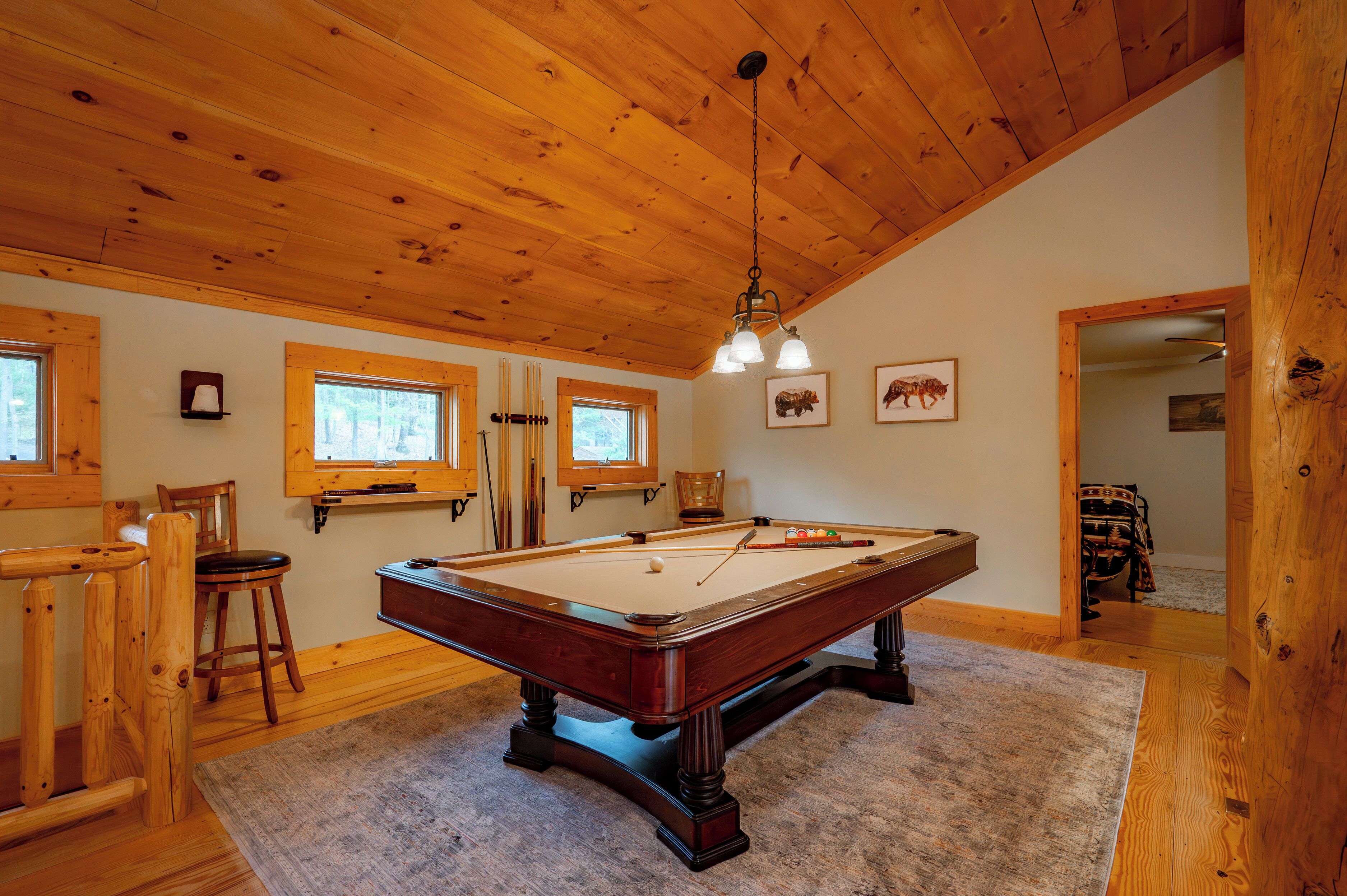 Une pièce aux murs lambrés, équipée d’une table de billard, de deux fenêtres et d’un luminaire au plafond.