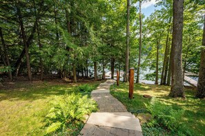 A stone pathway leading through a forested area with a lake in the background. - Mountain Air, Lake Days, Fireside Nights (Swanton)