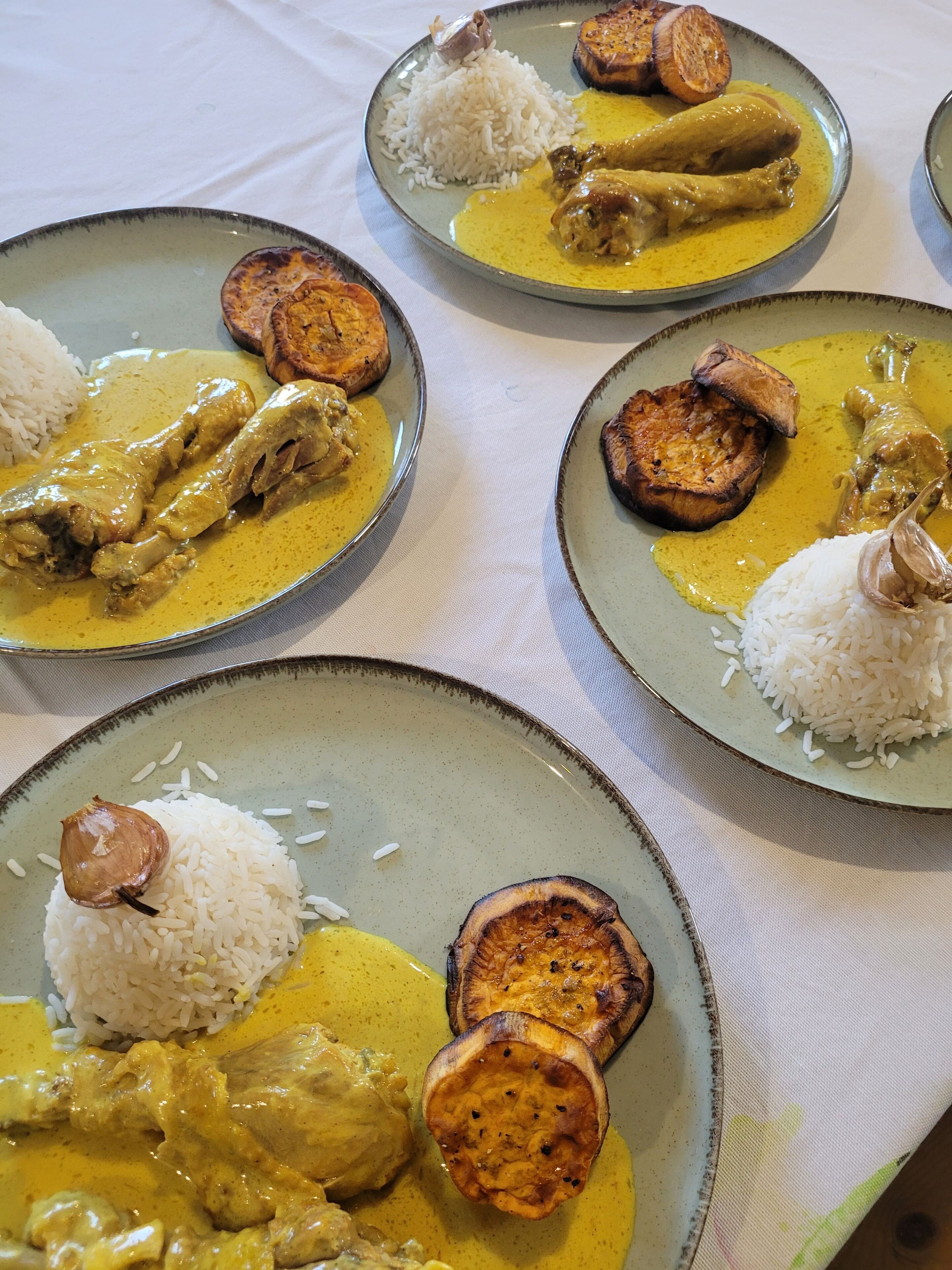 A table with plates of food, including rice, chicken, and slices of what appears to be roasted or grilled meat.