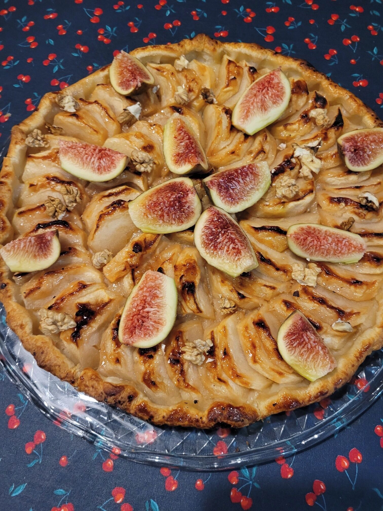 A round fruit tart with sliced figs and walnuts on a clear glass plate.