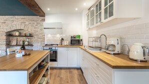 A modern kitchen with white cabinets, a wooden countertop, a stone wall, and various appliances. - Well-being house by the river (Cenans)