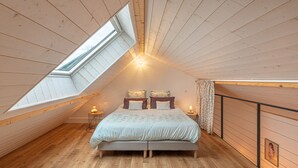 A cozy attic bedroom with a skylight, wooden walls, a bed with floral bedding, and two bedside lamps. - Well-being house by the river (Cenans)