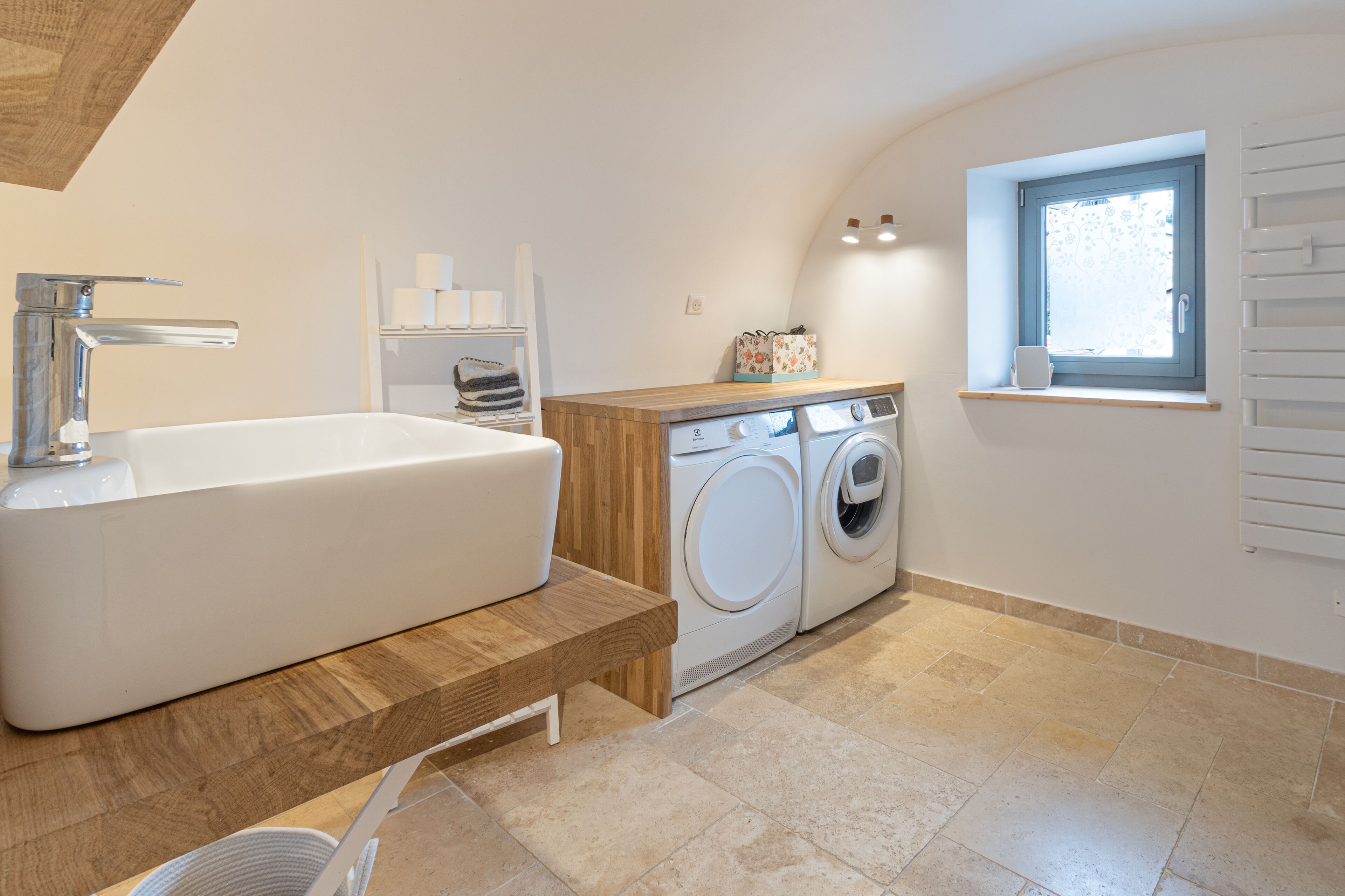 Ein modernes Badezimmer mit freistehender Badewanne, einer Waschmaschine und einem Fenster mit Jalousien.