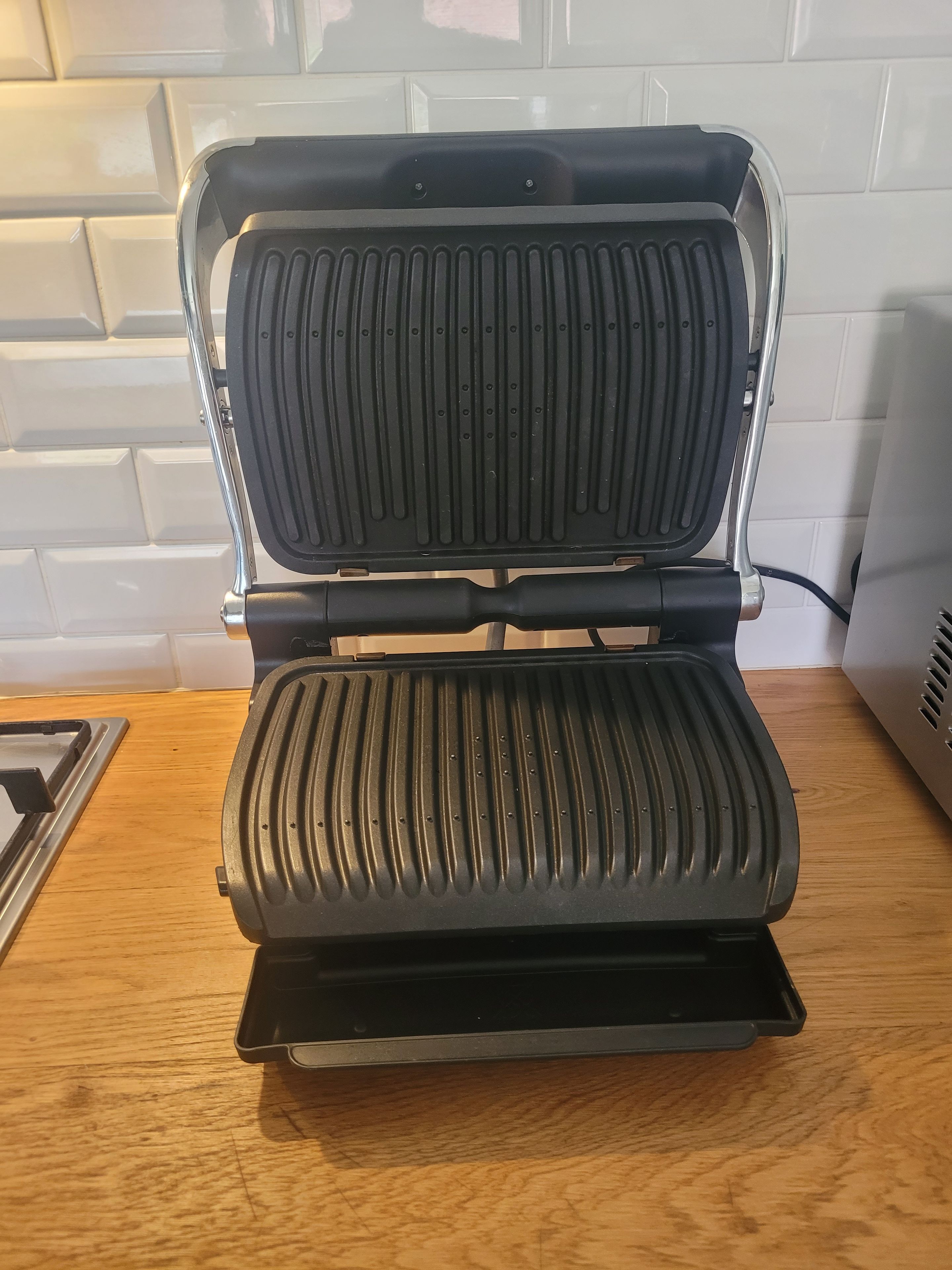 A sandwich grill with a metal frame and a black grill surface.