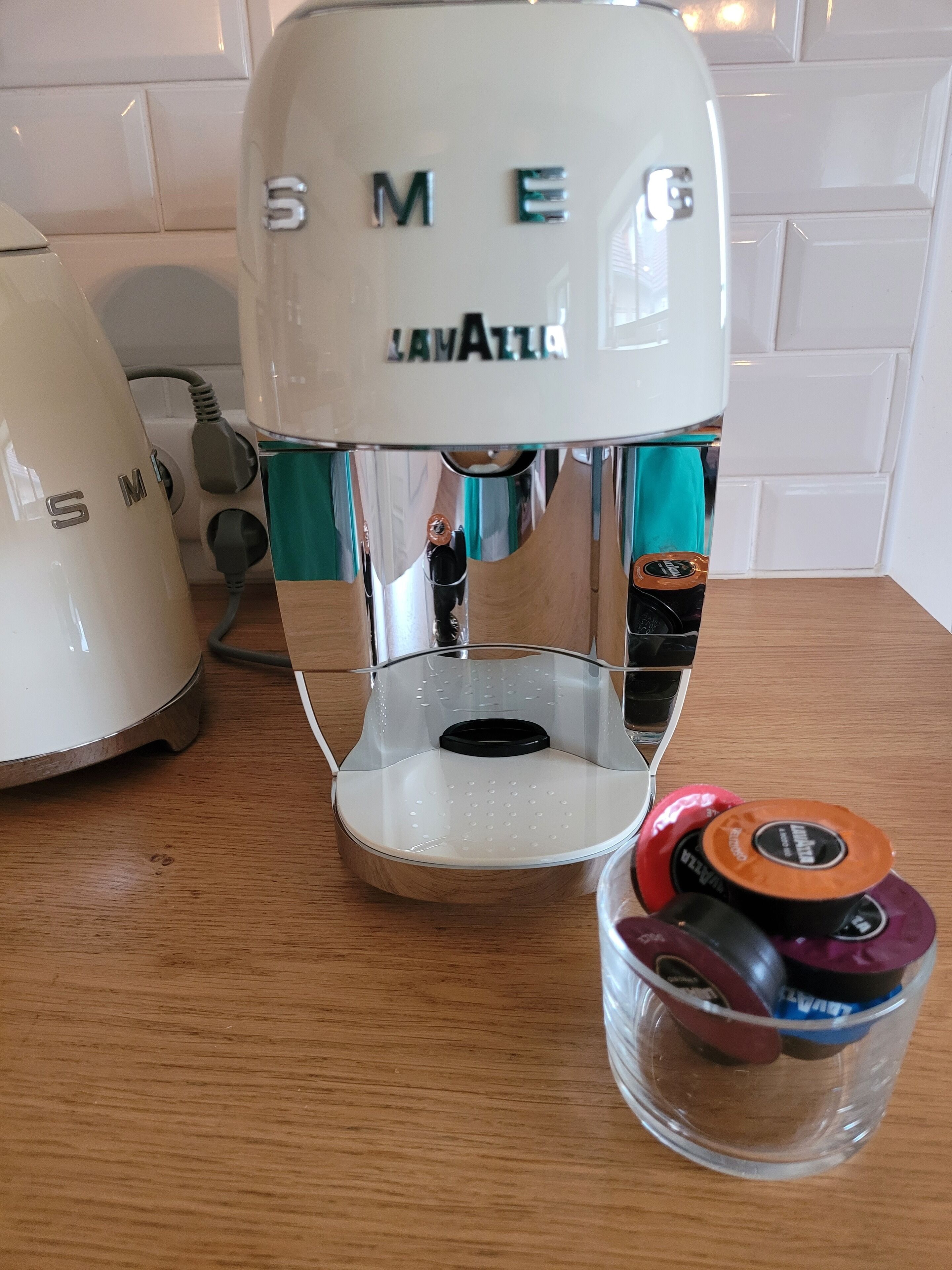 A white coffee maker with the brand name 'SMEG' and 'LAMATTA' visible on it, placed on a wooden surface.