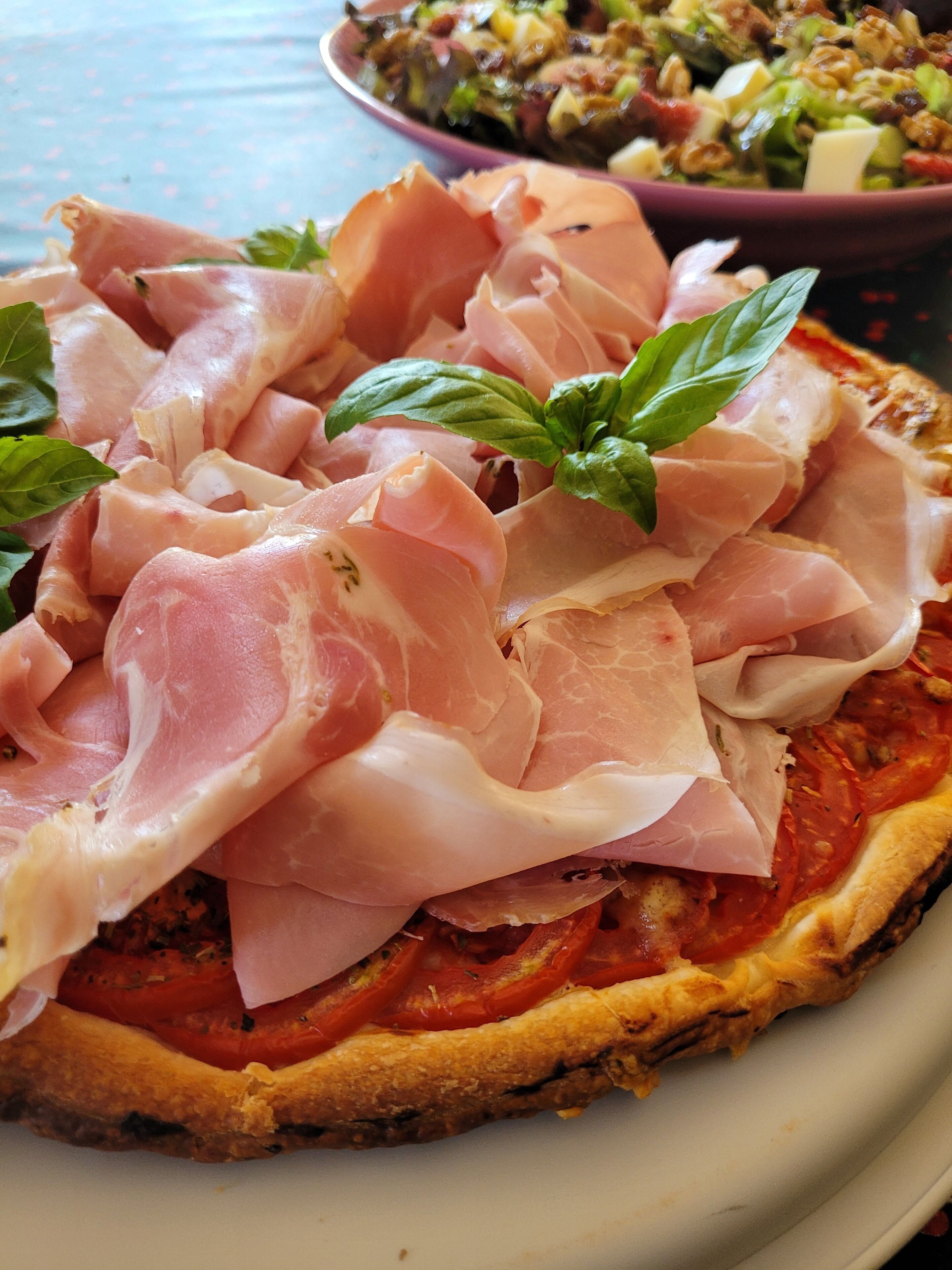 A pizza topped with prosciutto and fresh basil leaves.