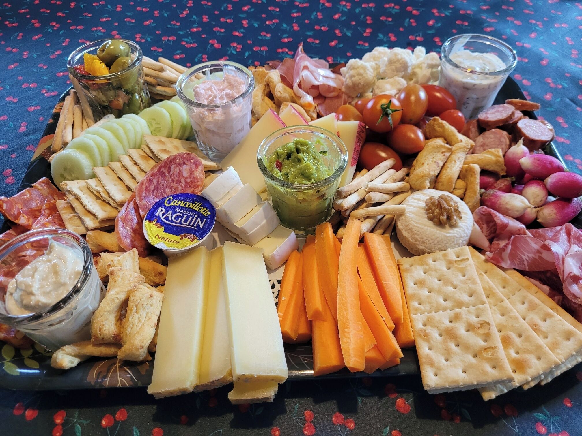 Un tagliere con formaggi, salumi, frutta e salse assortite.