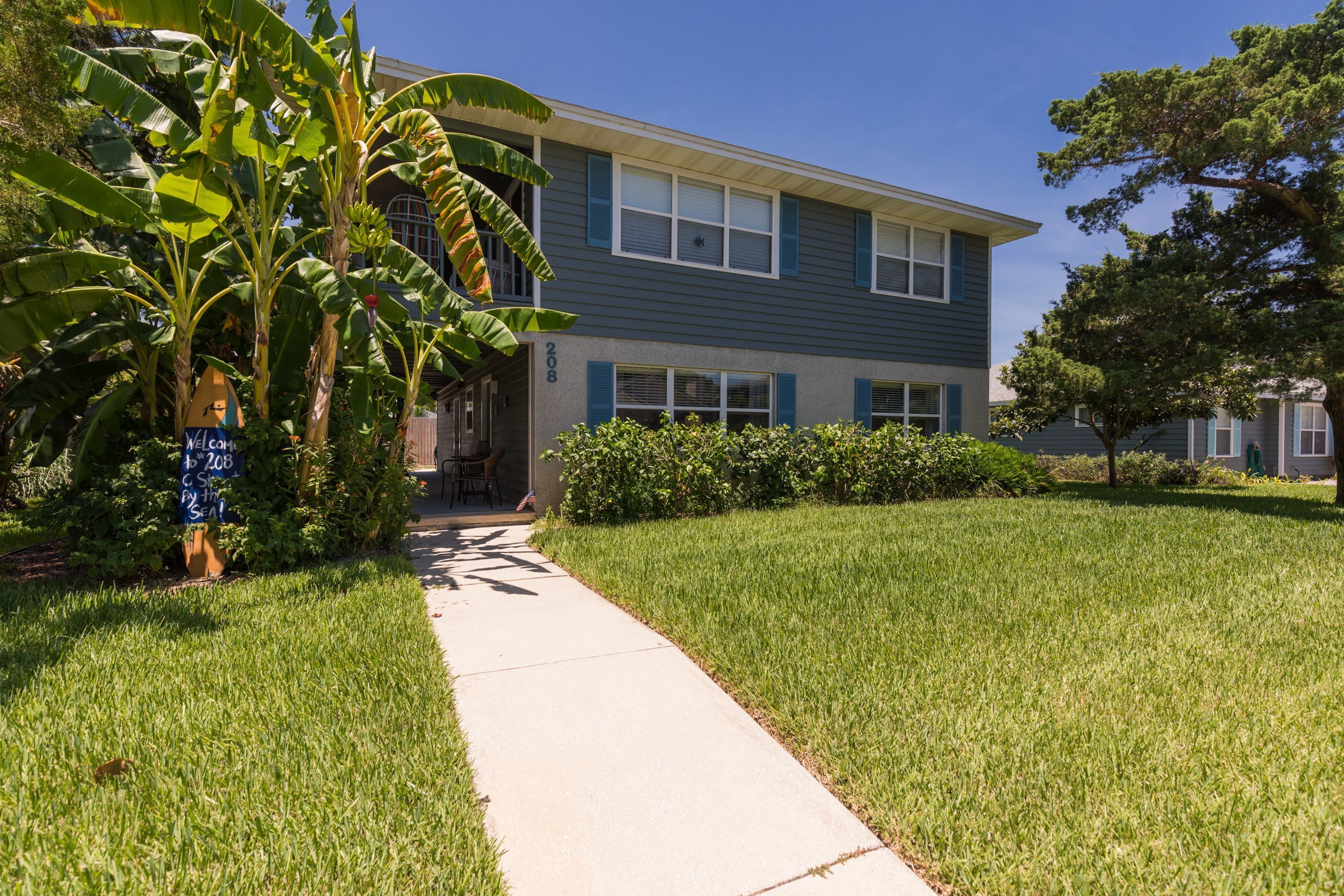 A two-story residential building with a well-maintained lawn and a pathway leading to the entrance.