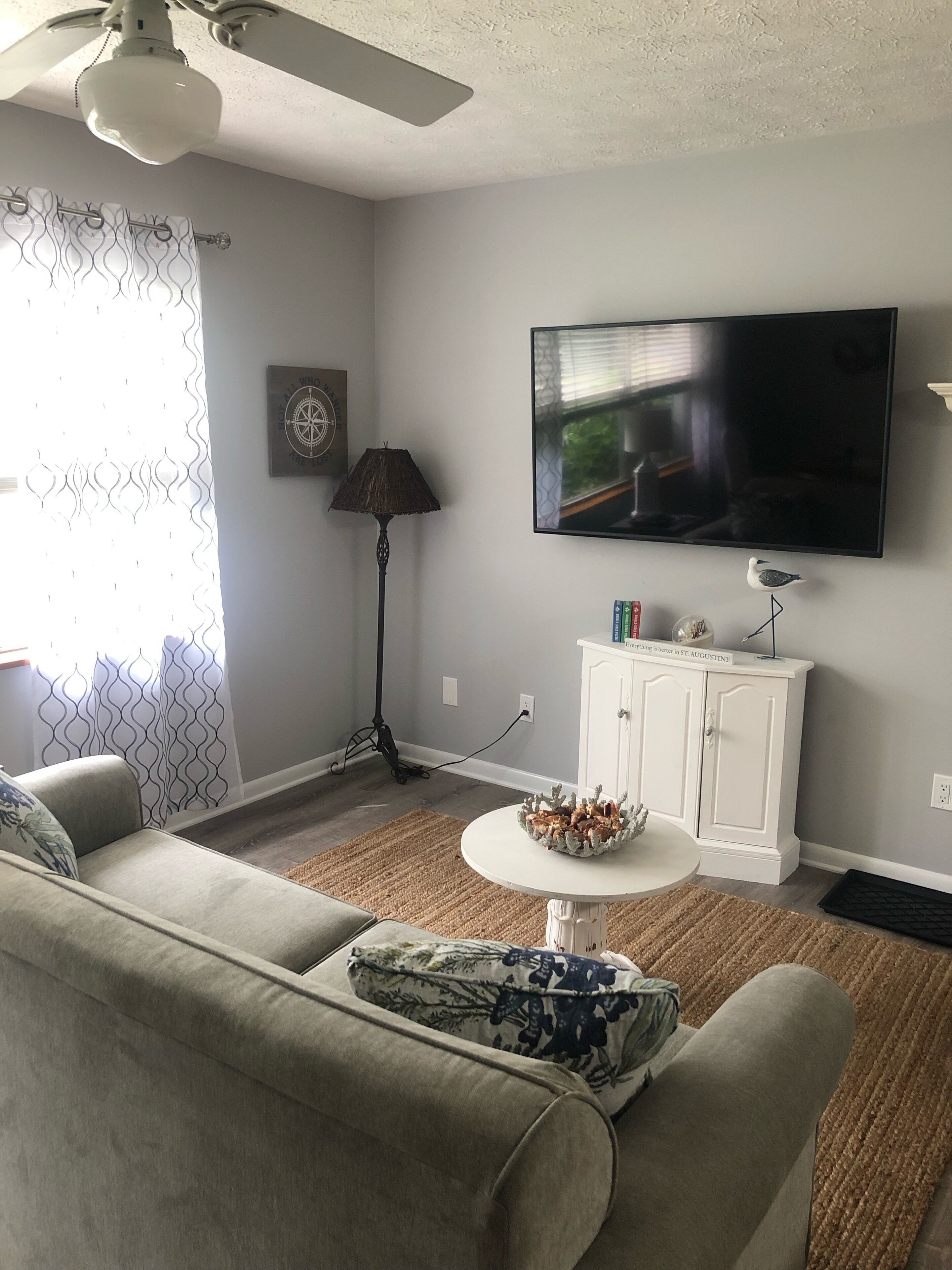 Uma sala de estar com ventoinha no teto, TV de tela plana, um armário branco e um tapete estampado.