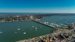 An aerial view of a marina with numerous boats docked, a bridge connecting the marina to the mainland, and a coastal town with visible buildings and roads. - Beachy Getaway–Cozy, Clean & Equipped w/ All Essentials! Relax, Enjoy & Refresh! (St. Augustine Beach)